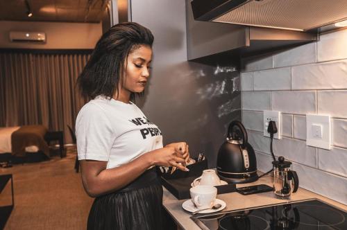 Uma mulher na cozinha a preparar uma chávena de café. em Blackbrick Sandton One em Joanesburgo