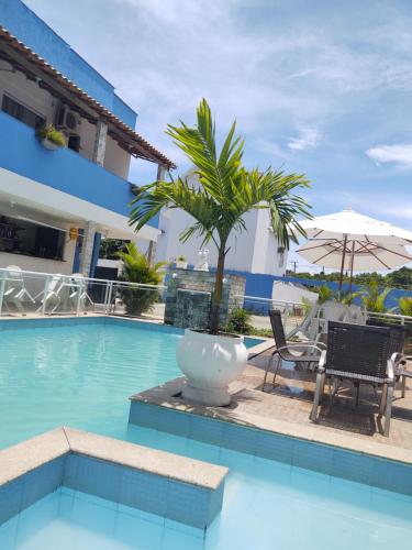 una piscina con sillas y una palmera junto a un edificio en Pousada Maresia Costa Azul, en Rio das Ostras