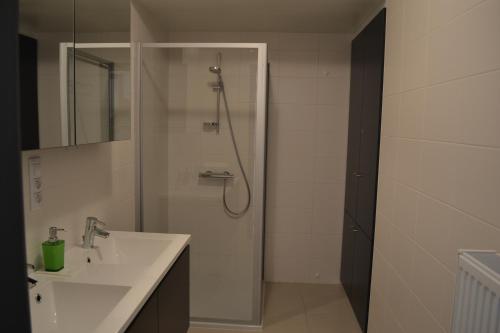 uma casa de banho branca com um chuveiro e um lavatório. em Margaux em De Panne