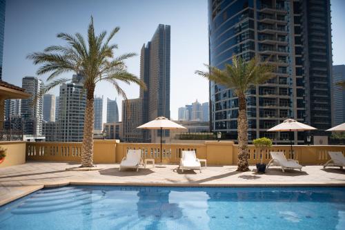 a swimming pool with chairs and palm trees on a building at Suha JBR Hotel Apartments in Dubai