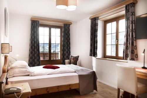a bedroom with a bed and a desk and windows at Hotel Waldhaus am See in Valbella