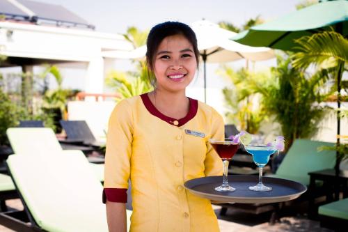 a woman holding a tray with two cocktails on it at Cheathata CTA Hotel Siem Reap in Siem Reap