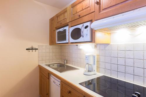 Elle comprend une petite cuisine avec des placards en bois et un évier. dans l'établissement Vacancéole - Résidence Le Sappey - Les 2 Alpes, à Les Deux Alpes