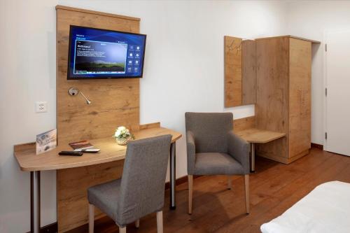 Habitación con escritorio, 2 sillas y TV en la pared. en Hotel Roggen en Erschmatt