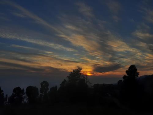 a sunset in the sky with trees in the foreground at Maa Anand Mayee Guest House in Panuānaula