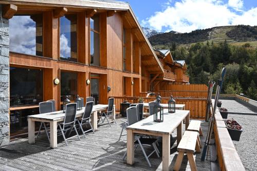 une terrasse en bois avec des tables et des chaises devant un bâtiment dans l'établissement Parc Madeleine - CHALETS, à Saint-François-Longchamp