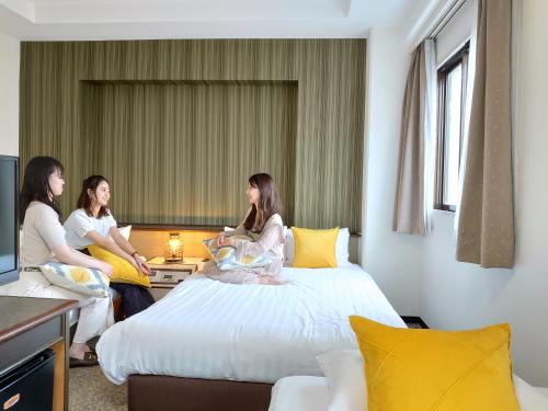 three women sitting on a bed in a hotel room at Hotel Area One Oita in Oita