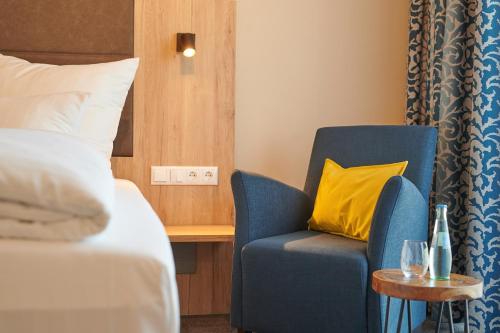 a room with a bed and a blue chair with a yellow pillow at Kucher's Landhotel in Darscheid
