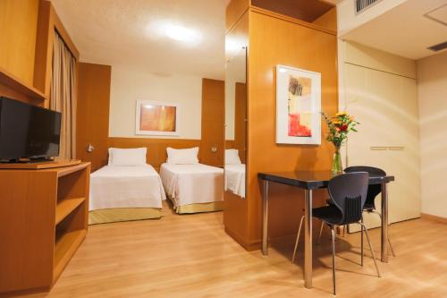 a hotel room with a bed and a desk and a tv at Nobile Suítes Uberlândia in Uberlândia