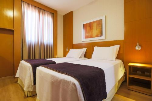 a hotel room with two beds and a window at Nobile Suítes Uberlândia in Uberlândia