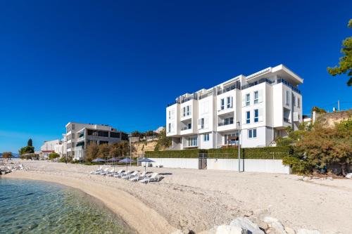 a white building on a beach with chairs and the water at Apartments Tanita in Podstrana