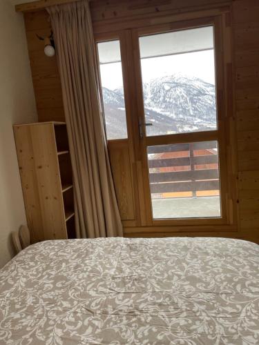 une chambre avec un lit et une grande fenêtre dans l'établissement Appartements à Chantemerle, à Saint-Chaffrey