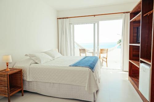 a white bedroom with a bed and a large window at Pousada Natureza in Morro de São Paulo