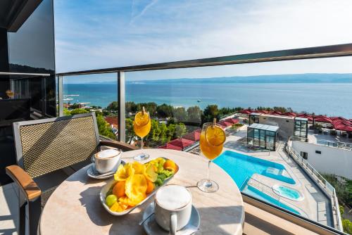 a table with a plate of fruit and wine glasses on a balcony at Hotel Plaža Duće in Duće