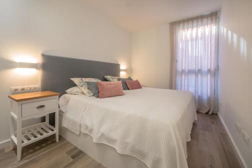 a white bedroom with a bed with a nightstand and a window at X-3 CALELLA DE PALAFRUGELL 6 PaX in Calella de Palafrugell