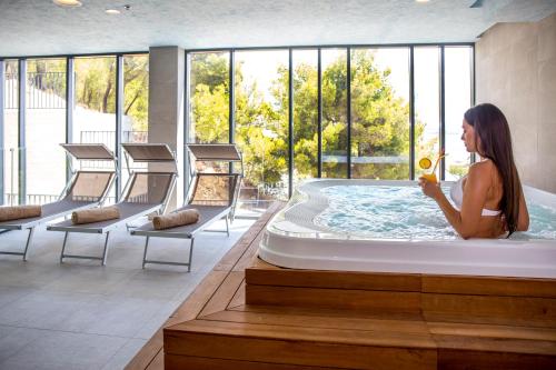 a woman in a hot tub in a room with windows at Hotel Plaža Duće in Duće