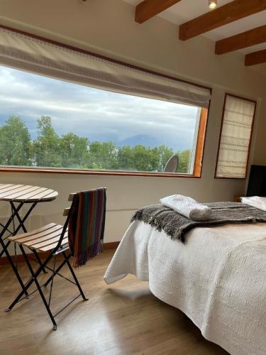 a bedroom with a bed and a table and a large window at Apart Hotel Sol y Lago in Pucón