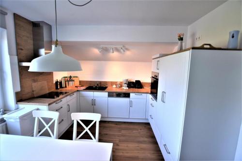 a white kitchen with white cabinets and white stools at Muschelkiste-H in Hohwacht