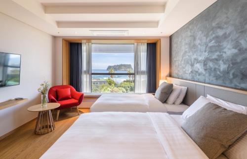 a hotel room with two beds and a red chair at The Grand Sumorum in Seogwipo