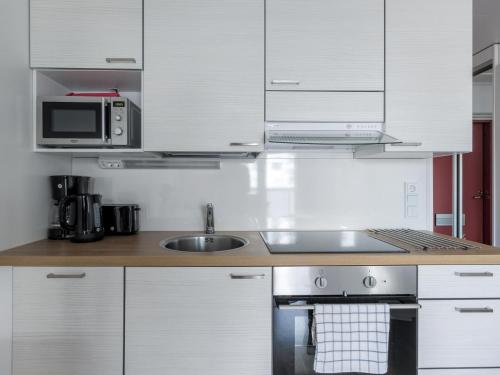 a kitchen with white cabinets and a sink and a microwave at Kotimaailma Apartments Joensuu - Koulukatu 21 in Joensuu