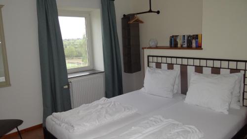een bed met witte lakens en kussens naast een raam bij Appartement Hoeve Espewey - Leisure only in Hombourg