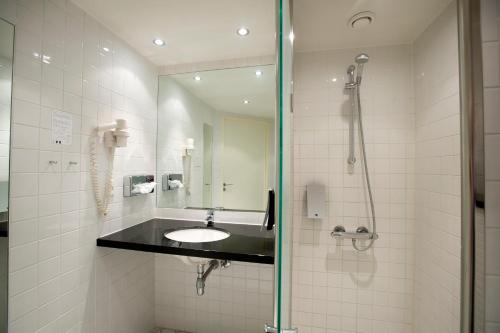 a bathroom with a sink and a shower with a mirror at Hotel Hedegaarden in Vejle
