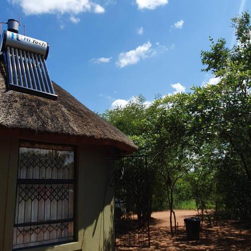 um edifício com telhado de palha com árvores ao fundo em Rhumbini Lodge em Malamulele
