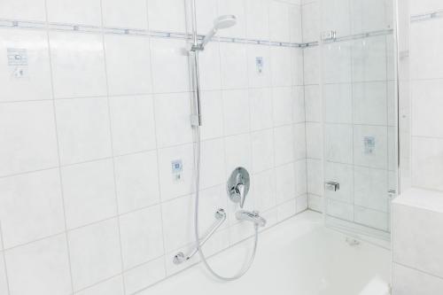 a shower in a bathroom with white tiles at HEIMATEL - Suiten, Apartments und Studios in Scheidegg