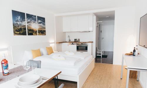 a white living room with a bed and a table at HEIMATEL - Suiten, Apartments und Studios in Scheidegg