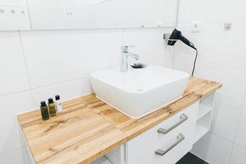 a white bathroom with a white sink on a wooden counter at HEIMATEL - Suiten, Apartments und Studios in Scheidegg