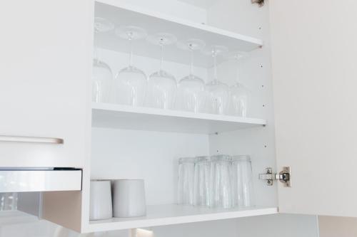 a white kitchen with clear glasses on a shelf at HEIMATEL - Suiten, Apartments und Studios in Scheidegg