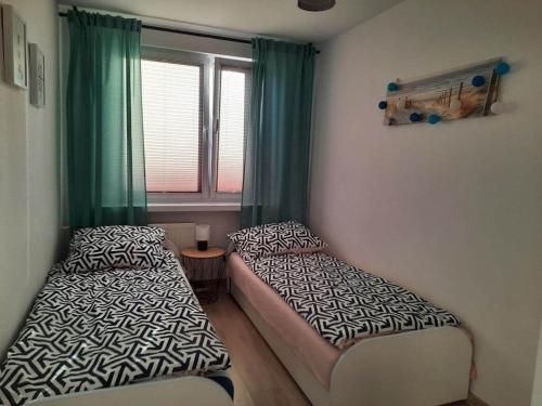 2 Betten in einem Zimmer mit grünen Vorhängen und einem Fenster in der Unterkunft Apartament Hel Leśna 8 in Hel