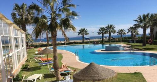 a swimming pool with umbrellas and palm trees and the ocean at Casa Salá, alojamiento con encanto en Vera Natura in Vera