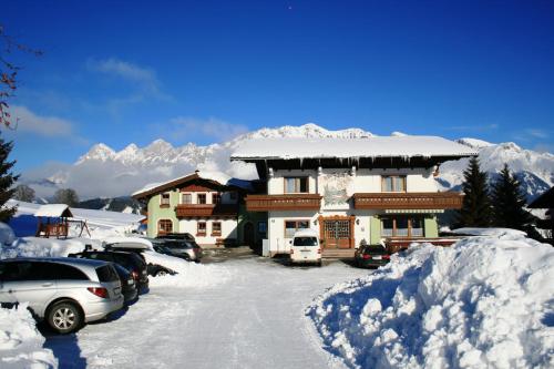 uma casa coberta de neve com carros estacionados num parque de estacionamento em Wellness-Pension Jagahütt'n em Schladming
