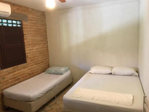 a bedroom with two beds and a brick wall at Casa de Veraneio, com piscina, churrasqueira, área de lazer, três suites com ar condicionado a 100m da praia, na Barra de São Miguel-AL in Barra de São Miguel