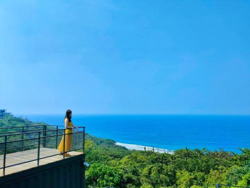 a woman in a yellow dress standing on a balcony looking at the ocean at 濱境行旅 Begin Inn in Xiaoliuqiu