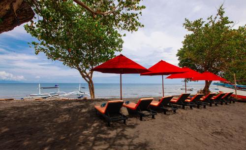 a row of chairs and red umbrellas on a beach at Bali Taman Lovina Resort & Spa Suites in Lovina