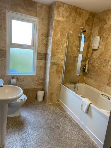 a bathroom with a tub and a toilet and a sink at The Kingswood Guest House - Adult Only in Weymouth