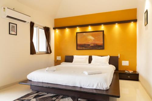 a bedroom with a white bed with a yellow wall at Villa Knox in Benaulim