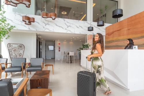 a woman is standing with a suitcase in a lobby at Hotel Água de Coco in Maceió