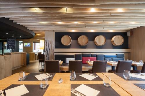 un restaurante con mesas de madera y barriles de vino en la pared en Ibis Aéroport Bâle Mulhouse en Saint-Louis