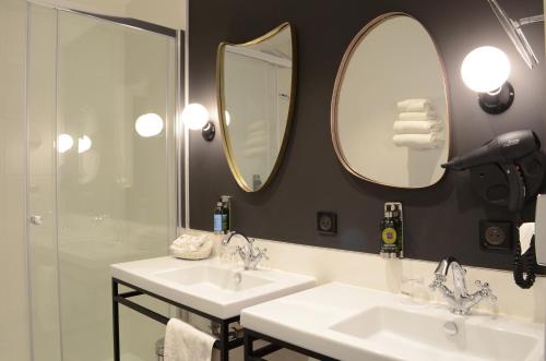 a bathroom with two sinks and two mirrors at Hôtel Anne d'Anjou, The Originals Collection in Saumur