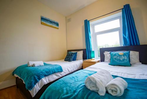 two beds in a room with blue curtains and a window at West Lea House in Chesterfield