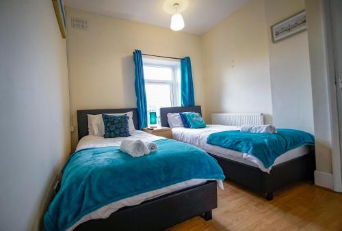 a bedroom with two beds with blue sheets and a window at West Lea House in Chesterfield