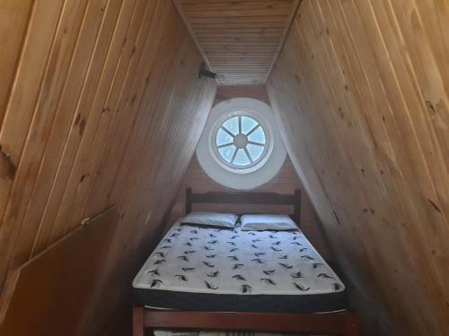 a small bed in a wooden room with a window at Chalés Monções in Ubatuba