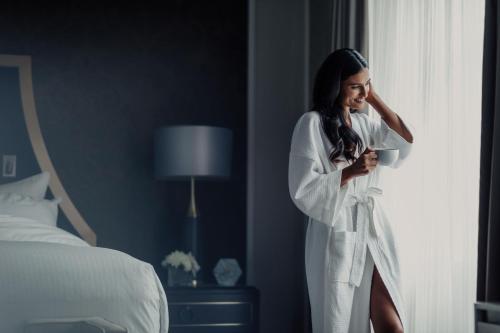 a woman in a white robe looking out of a window at Fairmont Hotel Vancouver in Vancouver