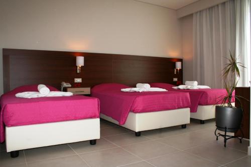 two beds in a hotel room with pink sheets at Matala Bay Hotel in Matala