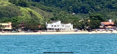 a white house on a beach next to the water at Solar Grego Pousada Ubatuba in Ubatuba