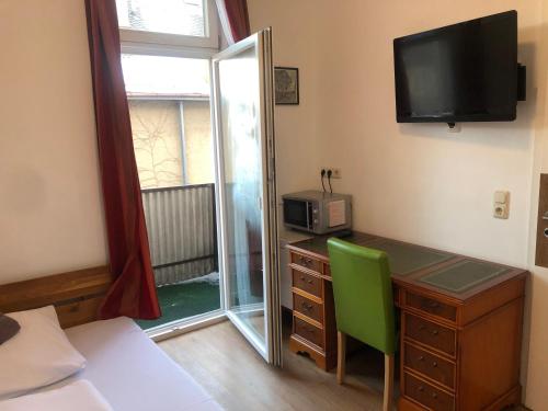 a bedroom with a desk with a green chair and a television at Hotel Pension Schmellergarten in Munich