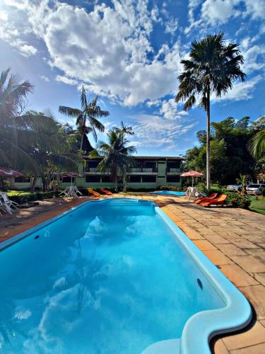 a large blue swimming pool with palm trees and a building at Hotel Jardim Tropical in Barcarena